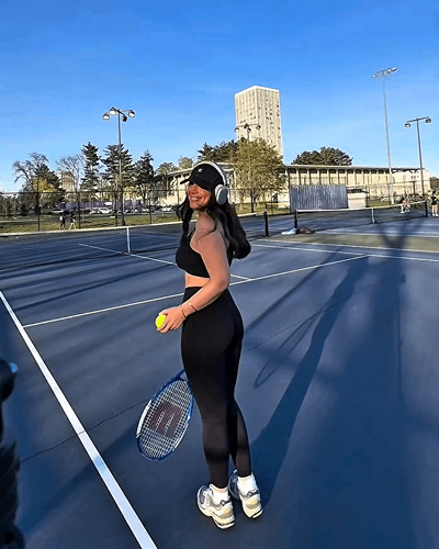 Woman wearing BRXL tennis outfit holding a racket and tennis ball on the court.