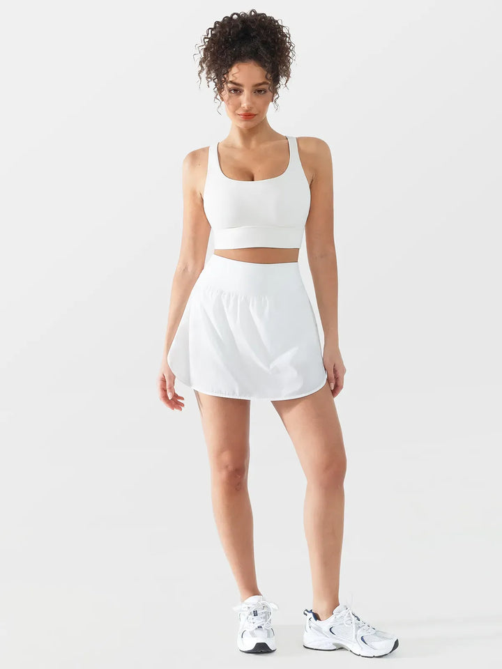 A model wearing a BRXL® Athletic High Waist Interior Pocket Tennis Skirt in