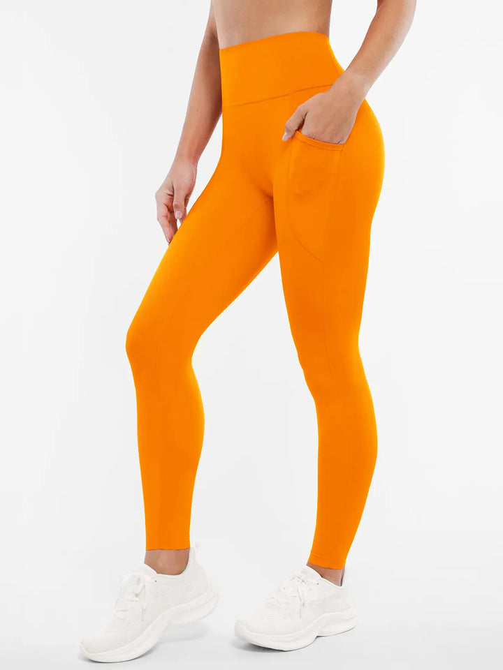 A model wearing a BRXL® BrxlZero™ High Rise Buttery Soft Yoga Leggings in Orange / XS