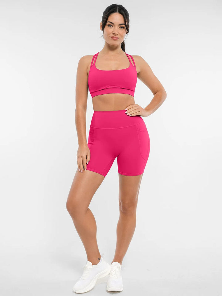 A model wearing a BRXL® Cross Strap Sports Bra High-Waisted Shorts Set in Set / Pink / XS