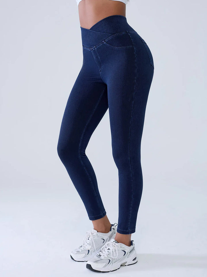 A model wearing a BRXL® Crossover Denim Sculpting Leggings with Pockets in Blue / XS