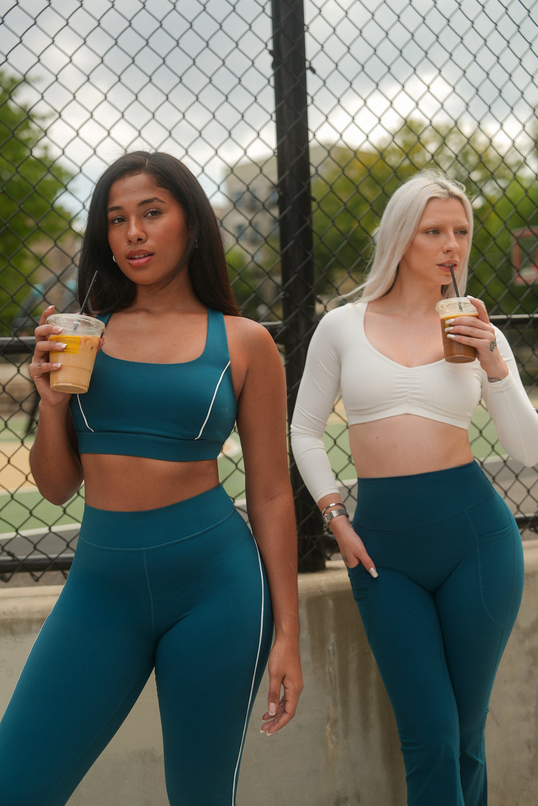 Two women in matching athletic wear holding drinks outdoors.
