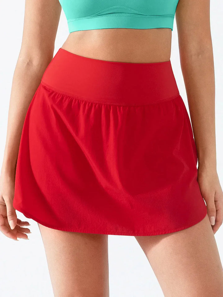 A model wearing a BRXL® Athletic High Waist Interior Pocket Tennis Skirt in