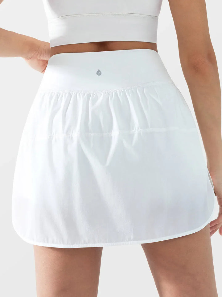 A model wearing a BRXL® Athletic High Waist Interior Pocket Tennis Skirt in