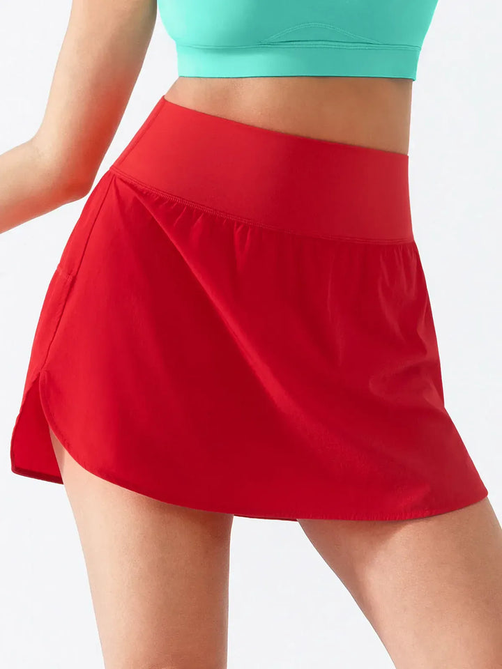A model wearing a BRXL® Athletic High Waist Interior Pocket Tennis Skirt in Red / S