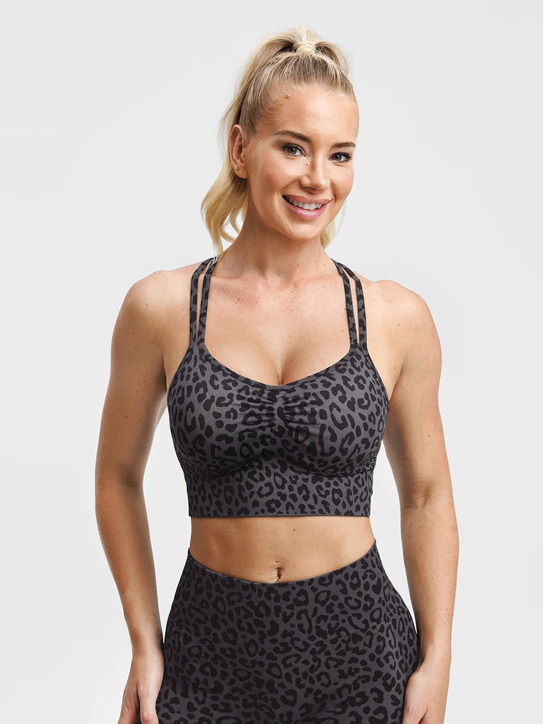 A model wearing a BRXL® B R X L® Seamless Criss Cross Spaghetti Racerback Sports Bra Grey Leopard / XS