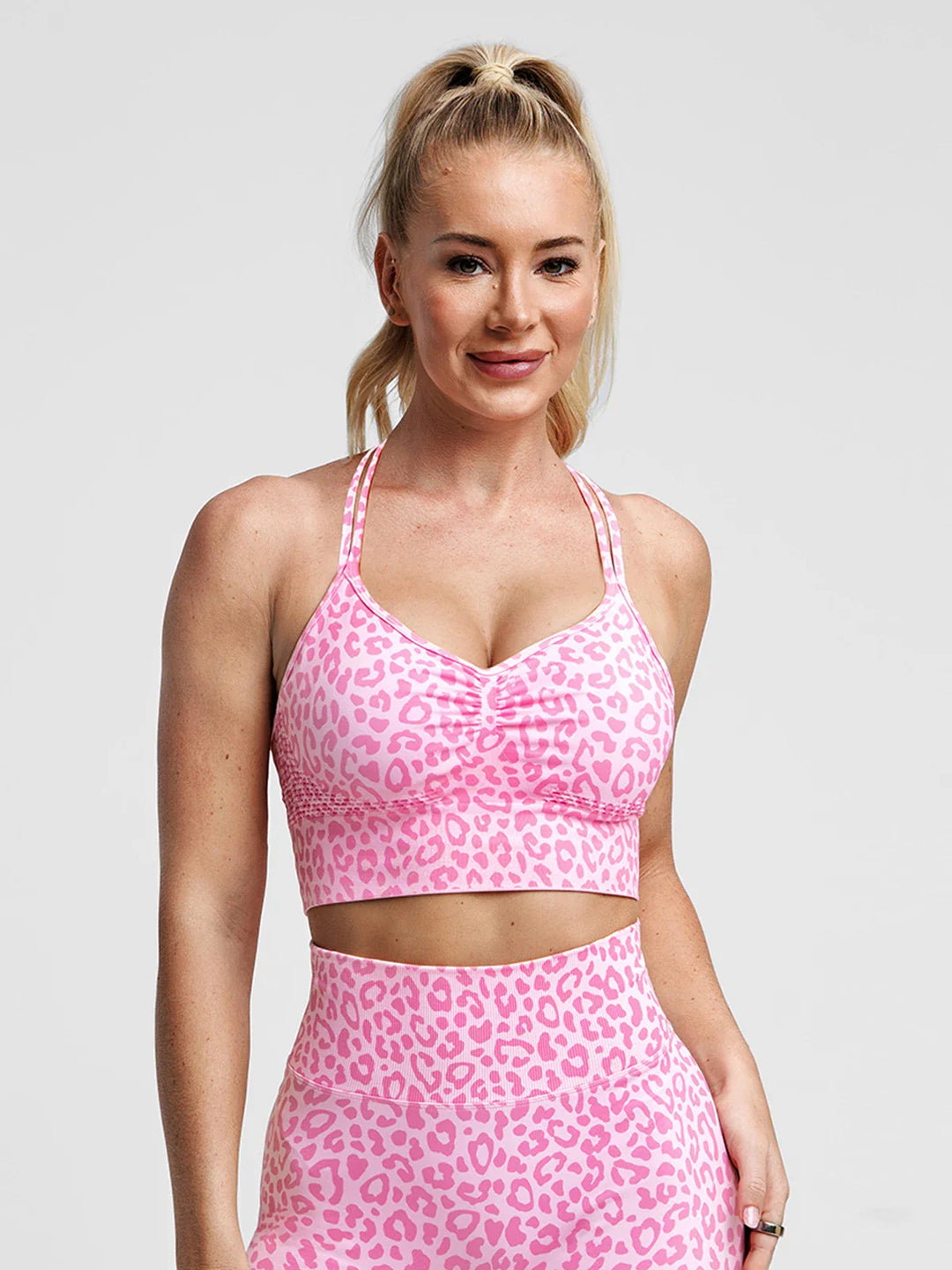 A model wearing a BRXL® B R X L® Seamless Criss Cross Spaghetti Racerback Sports Bra Pink Leopard / XS