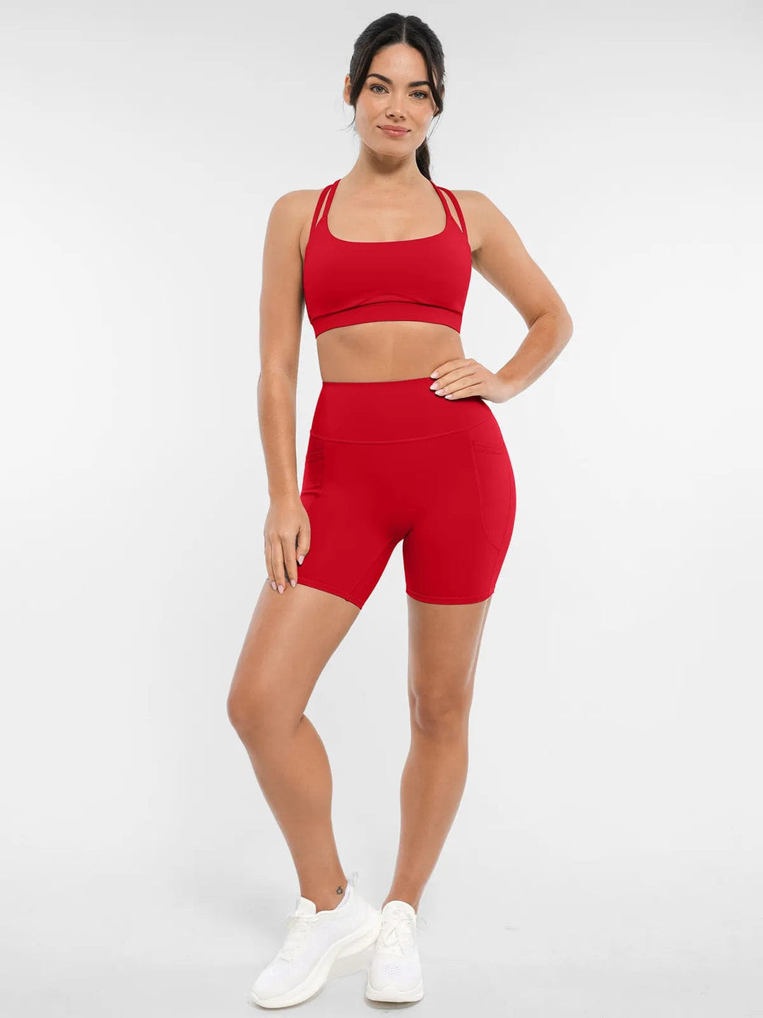A model wearing a BRXL® Cross Strap Sports Bra High-Waisted Shorts Set in Set / Red / XS