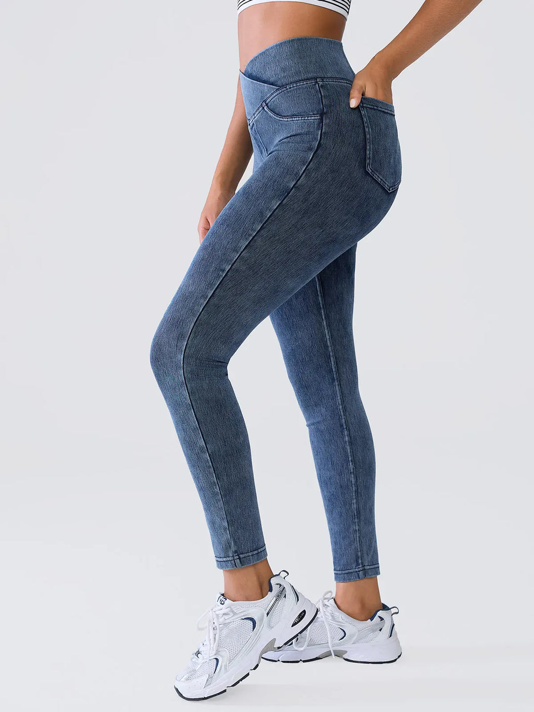 A model wearing a BRXL® Crossover Denim Sculpting Leggings with Pockets in Light Blue / XS